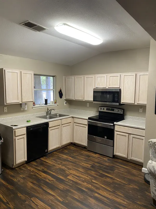 Kitchen with white cabinets, stainless appliances and dark plank flooring