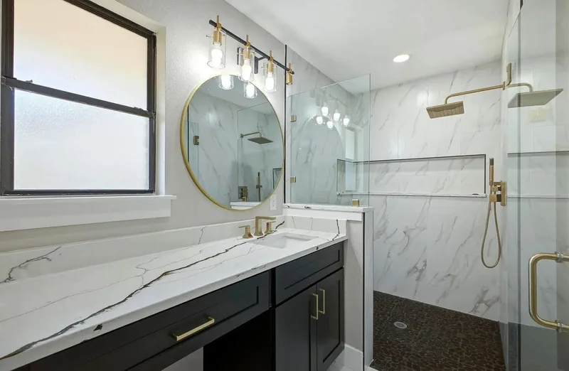 Bathroom vanity in white marble effect quartz with gold taps, beside a marble tiled walk in shower