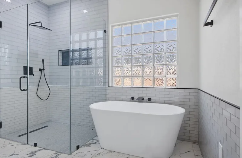 Freestanding tub beside a glass walk in shower, white subway tile and a glass block window