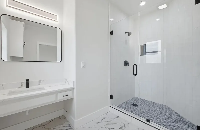 White bathroom with a long quartz vanity, black fittings and a glass shower with a mosaic floor