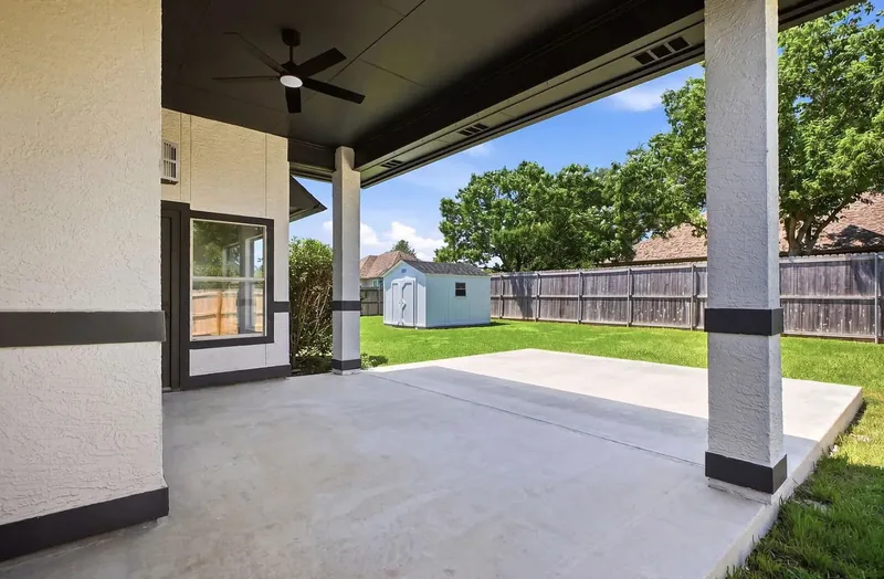 Poured concrete patio slab under a covered porch, looking out over a fenced back garden