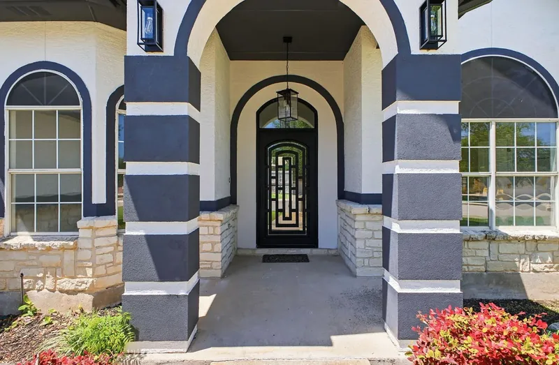 Arched stucco and stone entry porch with a black iron and glass front door