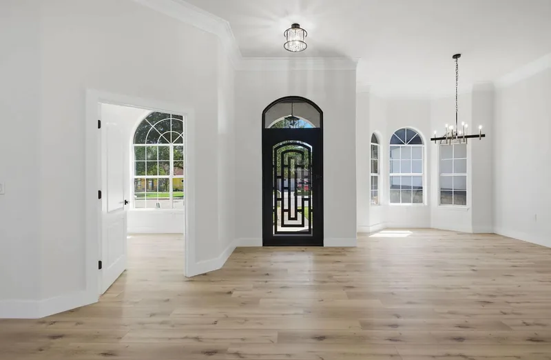 Wide plank oak flooring through an entry hall with an arched iron front door