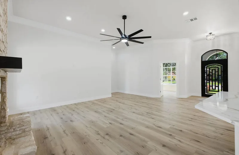 Living room with a stone fireplace, oak plank flooring and a large black ceiling fan