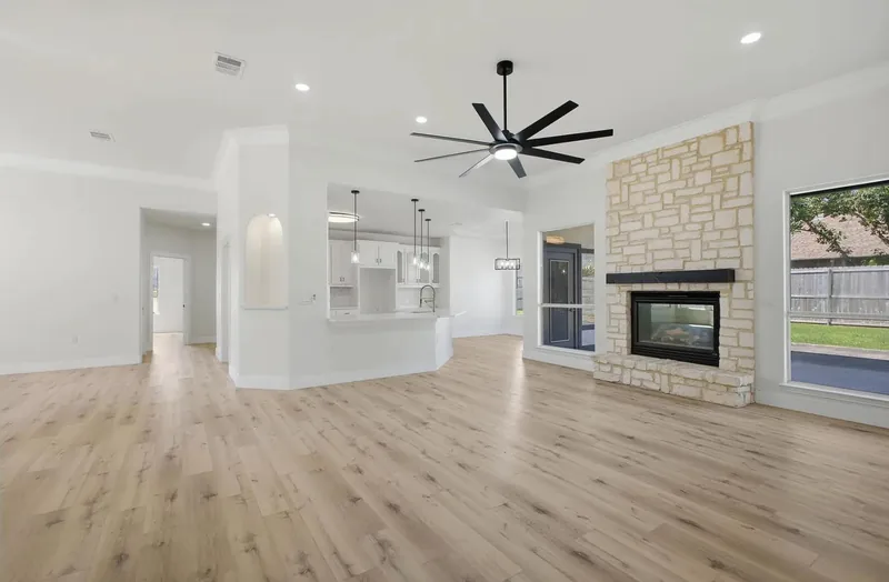 Light oak plank flooring running through an open living room and kitchen with a stone fireplace