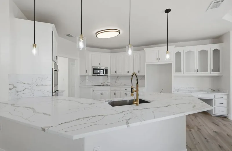 Kitchen island in white marble effect quartz with a gold tap, under glass pendant lights