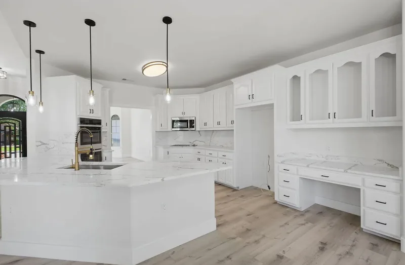 White kitchen with marble effect quartz counters, a built in desk and a wall oven