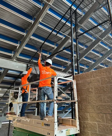 DFI crew on a scissor lift fixing chain link mesh to the steel frame under a grandstand