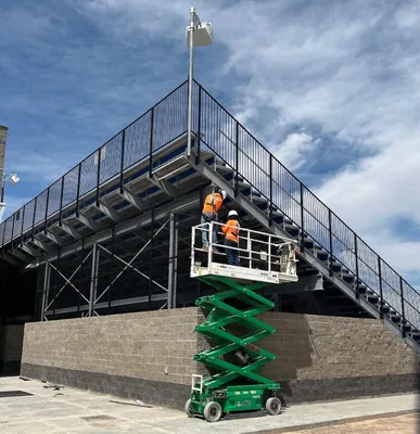Crew on a scissor lift working along the black railing on the end elevation of a grandstand