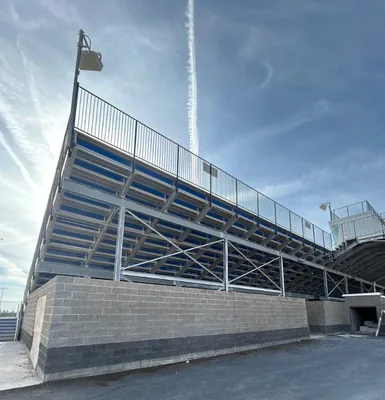 Finished grandstand with steel framing, blue seating and a black perimeter railing above a stone block wall